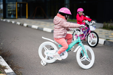 Two young children wearing helmets enjoy riding their colorful bicycles along a smooth pathway. The scene captures the joy and adventure of outdoor play and childhood exploration.の写真素材