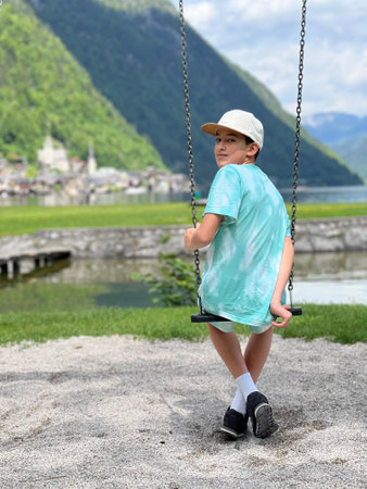 A young boy on a swing, capturing a moment of joy amid scenic mountains and serene water, perfect for depicting childhood and nature's beauty in Hallstatt, Austria.の写真素材