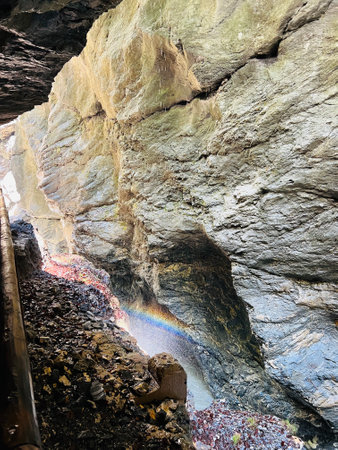 A serene rocky cavern illuminated by sunlight, showcasing a vibrant rainbow beneath a rugged rock face in Liechtensteinklamm, Austria. The natural beauty emphasizes the interplay of light and color within a cave setting.の写真素材