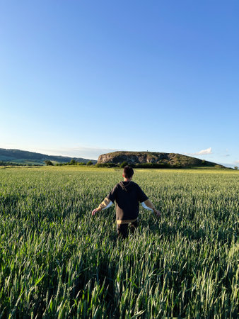 A person walks through a lush green field, arms outstretched, embracing nature's tranquility beneath a clear blue sky. The scene evokes freedom and connection with the outdoors.の写真素材
