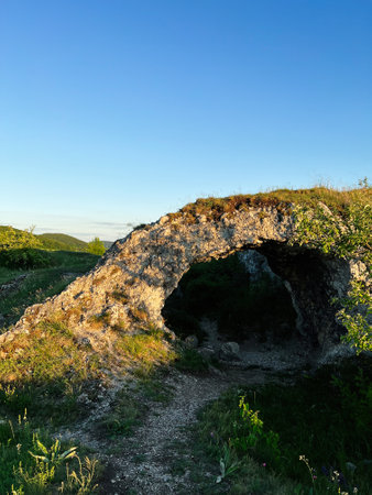 A stunning natural stone arch illuminated by the warm glow of sunset, set in a serene landscape with...
