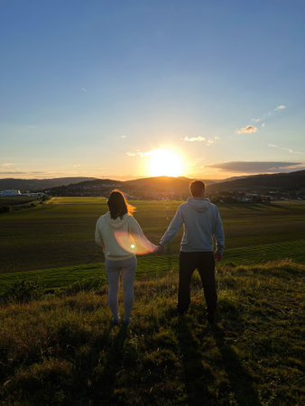 A couple stands hand in hand, gazing at a beautiful sunset over a vast, open landscape, creating a romantic and peaceful atmosphere.の写真素材