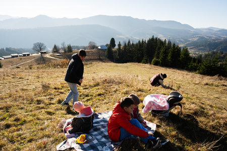 A family picnics on a hillside with stunning mountain views, capturing a peaceful outdoor day. Children play and relax, embracing the beauty of nature.の写真素材