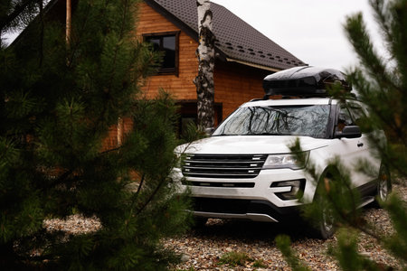A white SUV is parked in front of a rustic wooden cabin surrounded by green trees. Ideal for outdoor...