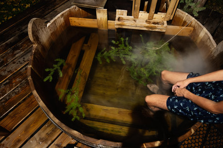 A person enjoying a soothing soak in a hot tub surrounded by natural wood. The steaming water creates a peaceful and calming atmosphere, offering a break from the daily routine.の写真素材