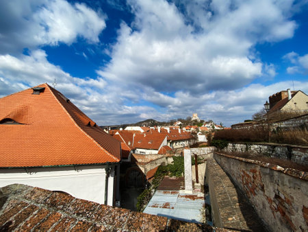 A picturesque scene of red-tiled rooftops in an old town, set against a dramatic cloudy sky in...