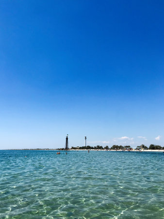 A beautiful clear blue ocean stretches towards a distant beach, under a sunny and cloudless sky in...