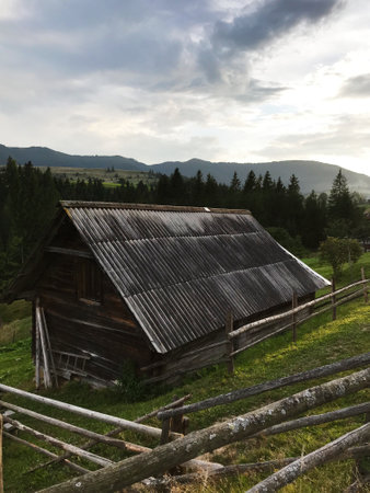 A rustic wooden barn nestled in a serene mountain countryside. Surrounded by lush greenery and wooden fences, it evokes a sense of solitude and natural beauty under a cloudy sky.の写真素材