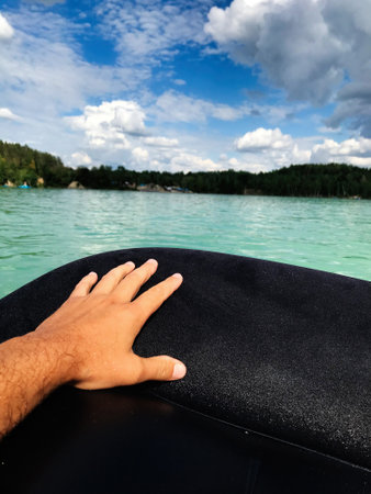 A man's hand rests on the edge of a boat, overlooking a serene lake, evoking feelings of tranquility...