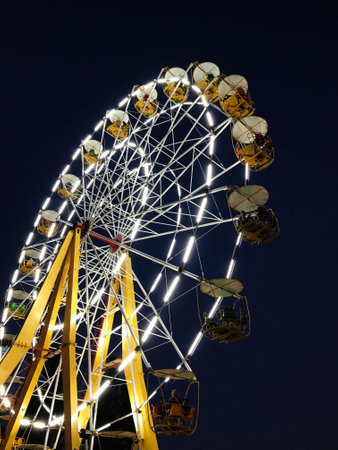 A brightly lit ferris wheel stands majestically against the night sky, creating a vibrant and magical mood perfect for amusement and adventure enthusiasts.の写真素材