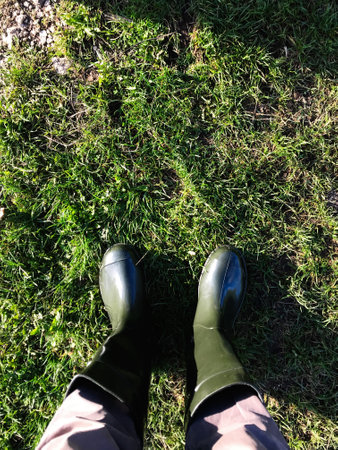 A person wearing dark green rubber boots stands on a lush green grassy path, capturing a moment of outdoor exploration. Ideal for themes of nature, adventure, and tranquility.の写真素材