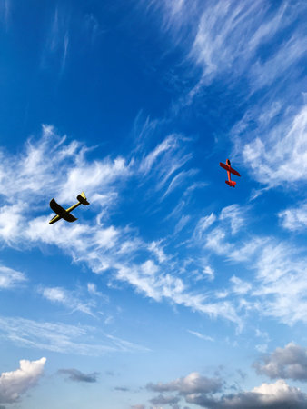 Colorful model airplanes glide through a vivid blue sky, set against a backdrop of airy, wispy...