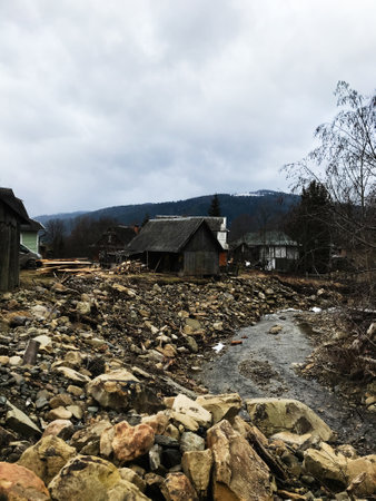 A rural scene featuring rocky terrain and rustic cabins with a mountain backdrop. The cloudy sky adds a moody atmosphere to this rugged, natural setting.の写真素材