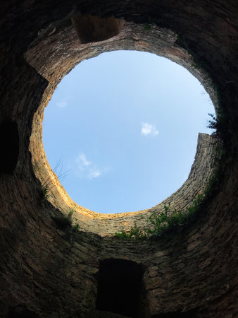 Looking up from inside a circular stone ruin, the opening reveals a clear blue sky. The ancient walls add a sense of history and mystery to this unique perspective.の写真素材
