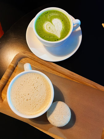 A cup of matcha latte with heart art, accompanied by a frothy coffee and a delicious macaroon on a...