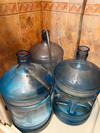 Image of three blue water jugs placed in a tiled bathroom corner, showing water storage in domestic...