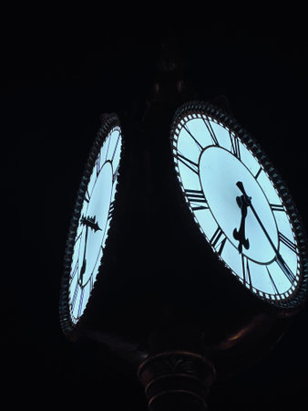 A striking image of an antique vintage clock glowing against a dark night sky, featuring detailed Roman numerals. The luminous clock face creates a mysterious and timeless ambiance.の写真素材