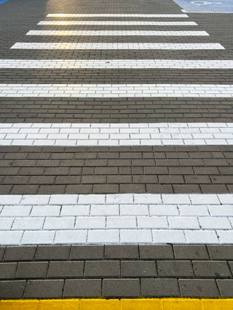 A detailed view of a pedestrian crosswalk on a brick pavement, highlighted by white stripes and a yellow curb. Ideal for urban planning and safety themes.の写真素材