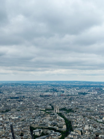 Aerial view of Paris cityscape featuring the iconic Arc de Triomphe surrounded by sprawling urban landscape under a cloudy sky.の写真素材