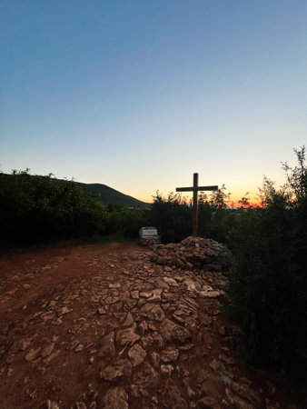 A scenic view of a rustic path with a wooden cross against a sunset backdrop, evoking tranquility...