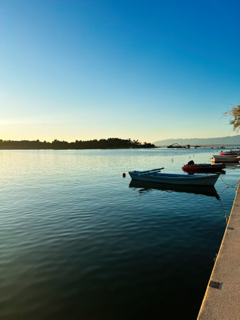 Evening scene depicting a serene sunset over a calm bay with moored boats. The still waters and...