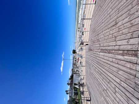 A peaceful beachfront boardwalk under a vibrant blue sky with neatly arranged empty beach chairs. The scene conveys tranquility and invites anticipation of summer beach activities.の写真素材