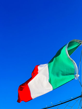 The vibrant Italian flag waves vividly against a clear blue sky, symbolizing national pride and...
