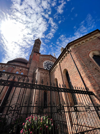 A stunning view of a historic cathedral with intricate brickwork and beautiful floral details under a vibrant blue sky with scattered clouds, showcasing architectural grandeur. Padua, Italy.の写真素材