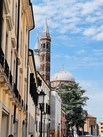 A beautiful street scene featuring historic architecture and prominent church towers under a bright blue sky. This image captures cultural heritage and architectural beauty. Padua, Italy.の写真素材