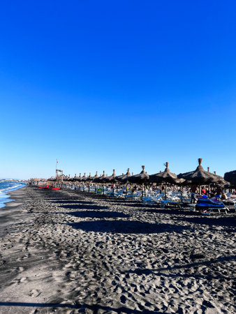 A picturesque sandy beach lined with straw umbrellas under a vibrant blue sky. The tranquil seaside setting offers a peaceful escape, ideal for relaxation and summer vacations. Manfredonia, Italy.の写真素材