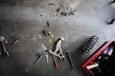 View of various car parts and tools scattered on a garage floor, showcasing a mechanical workspace....