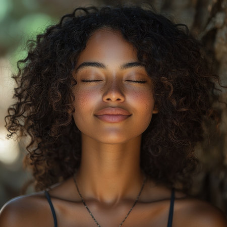 A peaceful portrait of a woman with curly hair and closed eyes, enjoying nature. The setting emphasizes tranquility, with soft sunlight and a background of natural greenery creating an ambient scene.の素材