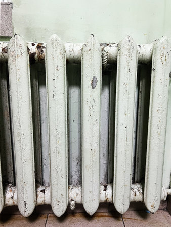 A vintage radiator with worn and peeling paint, set against a green wall and tiles. The image...