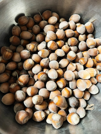 Unshelled hazelnuts placed in a metallic bowl, showcasing their natural textures and earthy colors...