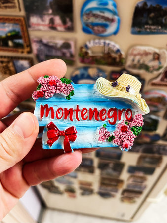 A hand displaying a bright Montenegro fridge magnet decorated with roses, a straw hat, and red accents. Ideal for representing travel souvenirs, cultural symbols, and memorable international destinations.の写真素材