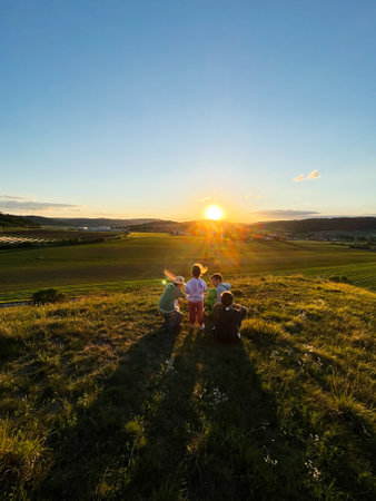 Group of people experiencing a serene sunset moment on a hill overlooking a vast green field.の写真素材