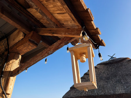 A rustic wooden lantern and lights dangling under a wood roof in bright daylight.の写真素材