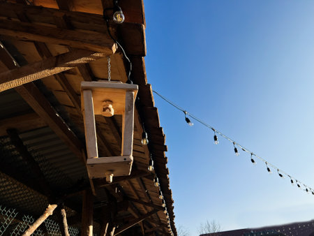 Hanging wooden lantern under a rustic roof with decorative lights and clear skyの写真素材