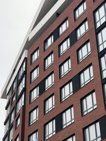 Contemporary brick apartment building with angled windows and architecture detail under cloudy sky