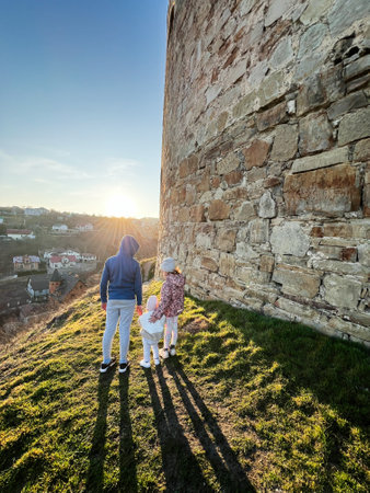 Kidsstanding near a rustic wall as the sun sets in the horizon.の写真素材