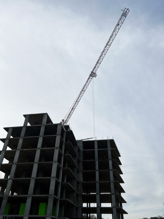 Partially built structure with a crane stretching up towards a cloudy atmosphere overheadの写真素材