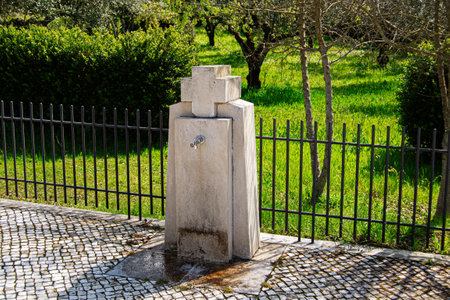 Ancient stone water fountain in Portugal surrounded by green grass and sunlight