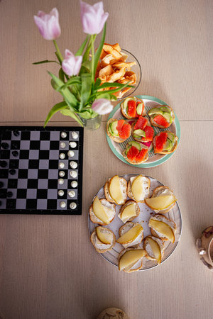 Plate of fruit snacks, chessboard, chips, and flowers creating a casual settingの写真素材