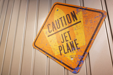 Yellow caution sign indicating jet plane proximity, displayed on a metal wall surface.の写真素材