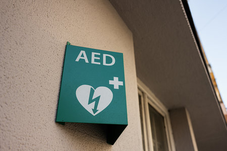 Green AED defibrillator sign on building wall, showcasing emergency medical equipment location.