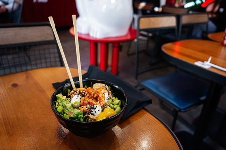Poke bowl with shrimp and fresh ingredients on a wooden table in a restaurantの写真素材