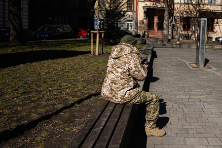 Soldier wearing camouflage clothing sitting on a bench in a public park in Lviv, Ukraine.の写真素材