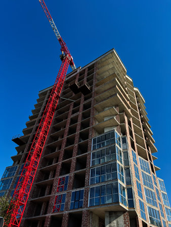 A skyscraper under construction featuring a red crane against a bright blue sky