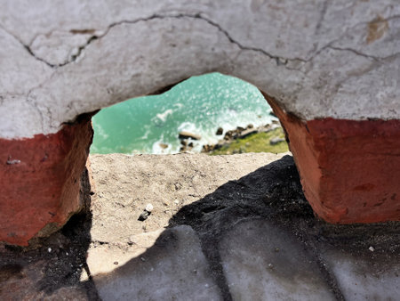 Turquoise water seen through an aged stone wall opening in Nazare, Portugalの写真素材