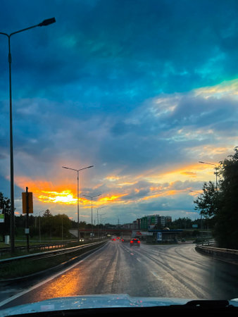 Wet road reflects city lights under a vibrant, dramatic sunset during twilight hour.